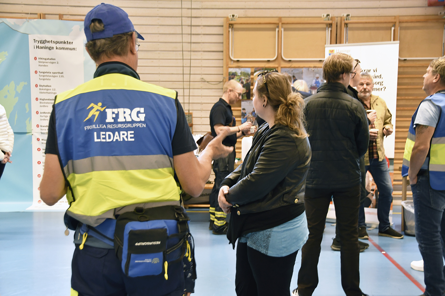 En person i väst märkt 'FRG FRIVILLIGA RESURSGRUPPEN LEDARE' samtalar med deltagare vid invigningen av trygghetspunkter.