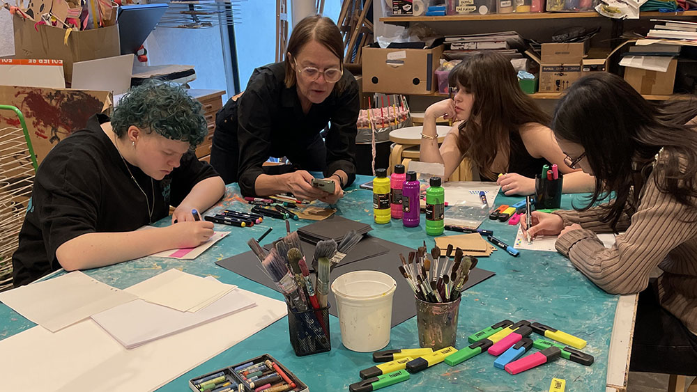 Ungdomar och vuxen person som skapar konst tillsammans runt ett bord