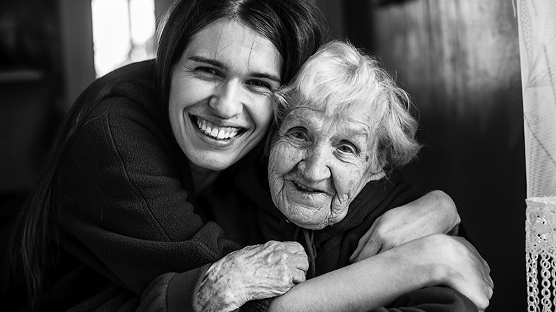 Äldre kvinna sitter bredvid en ung man. Båda ler.