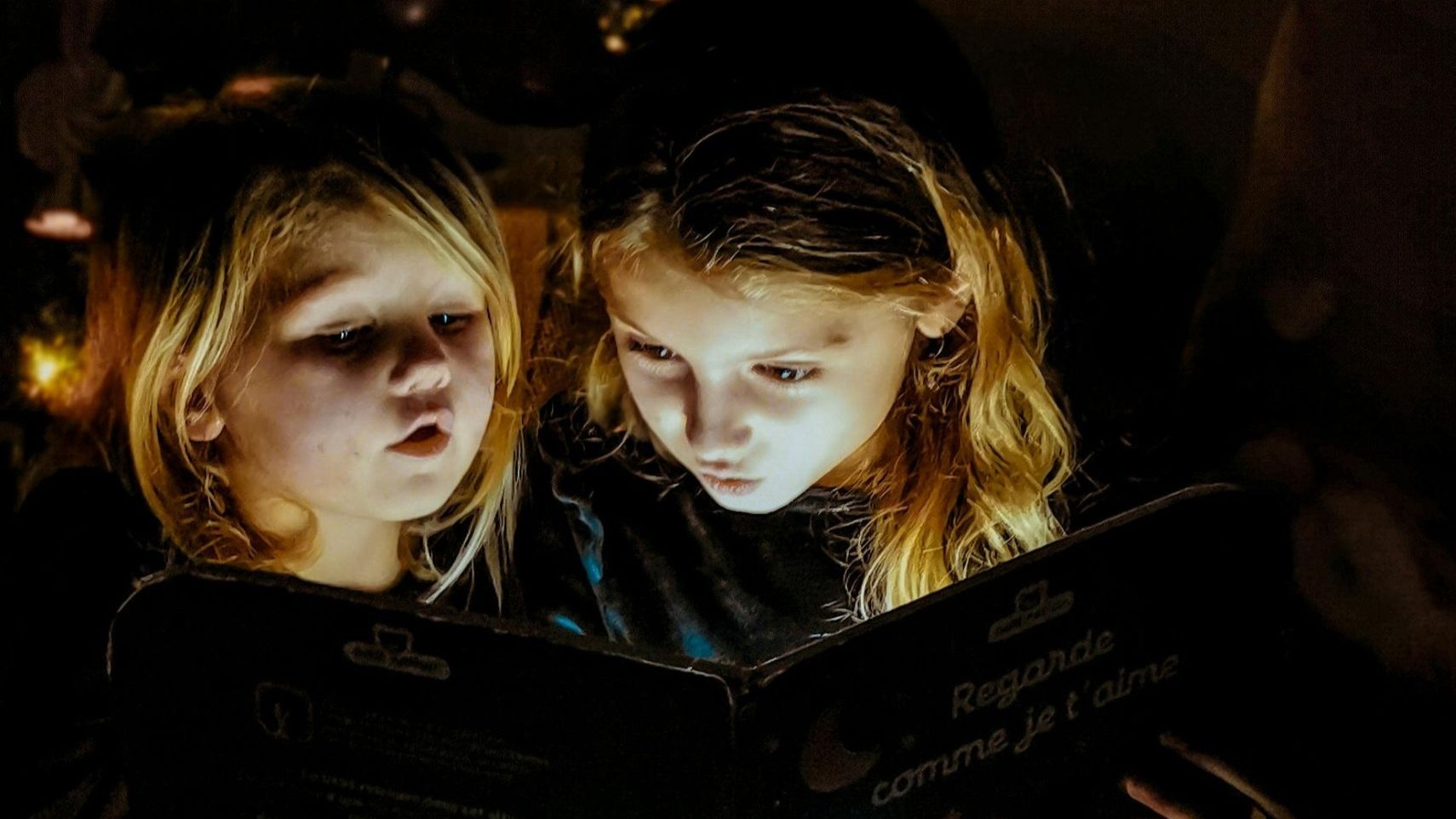 Bild på två flickor som sitter i mörkret och läser en bok tillsammans