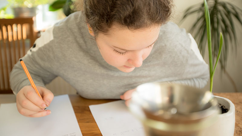 En ung tjej sitter böjd över ett bord och skriver på ett papper