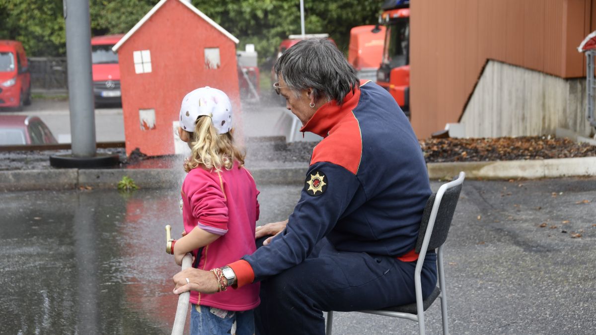 Flicka provar brandslang med hjälp av en brandman.