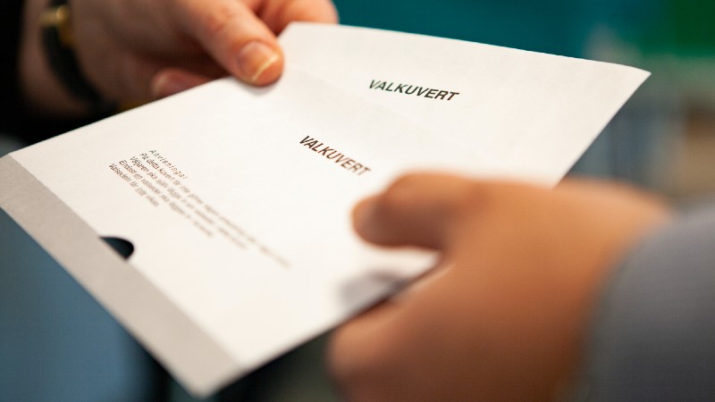 Närbild på röstkuvert som lämnas över till röstmottagare