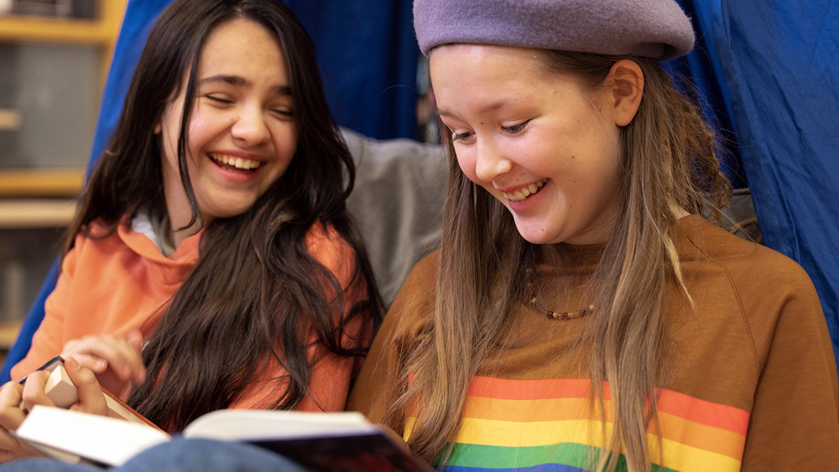 Två tjejer skrattar och tittar ner i en bok.
