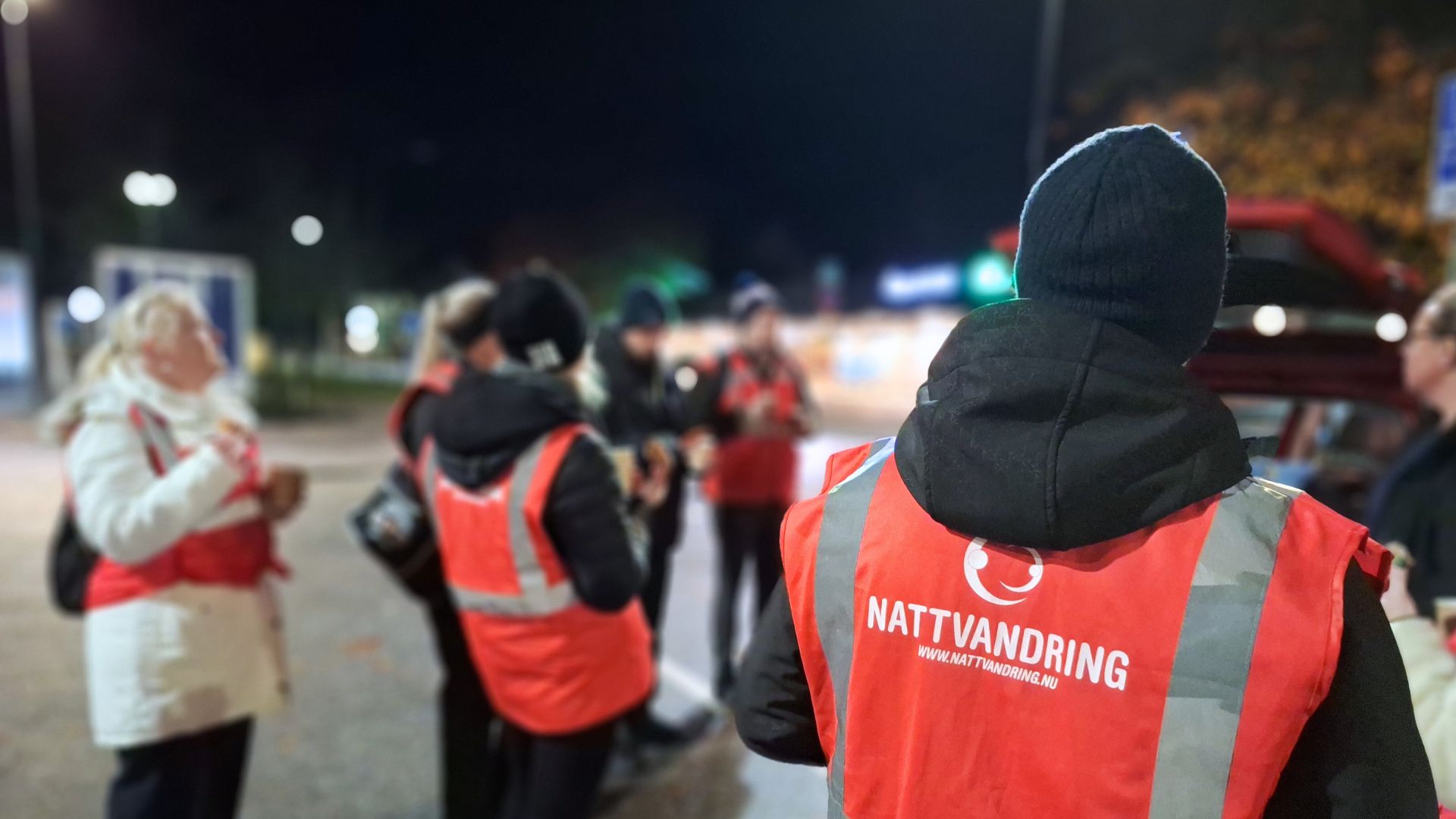 En grupp vuxna med rosa reflexvästar samlas kvällstid inför att trivselvandra.