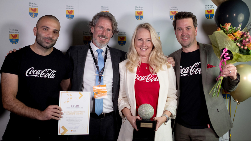 Tre representanter från Coca Cola fotade framför en fotovägg tillsammans med Sven Gustafsson. Diplom, ballonger och pris syns i bildr 