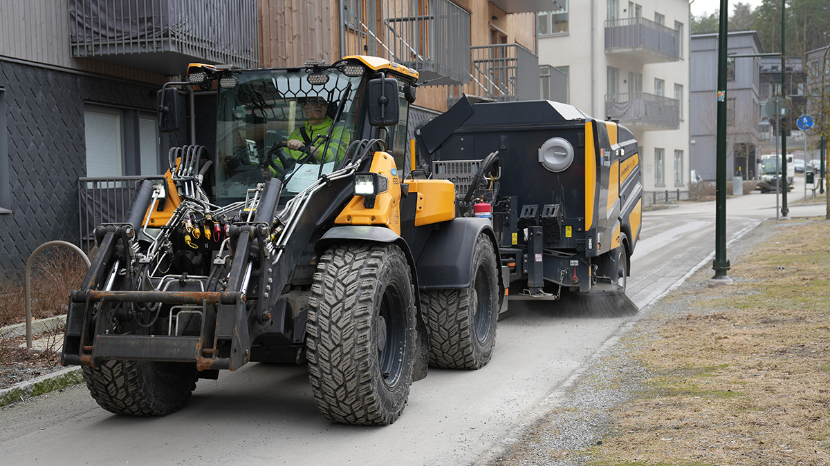 Traktor sopar upp sand på en gångväg i Vega