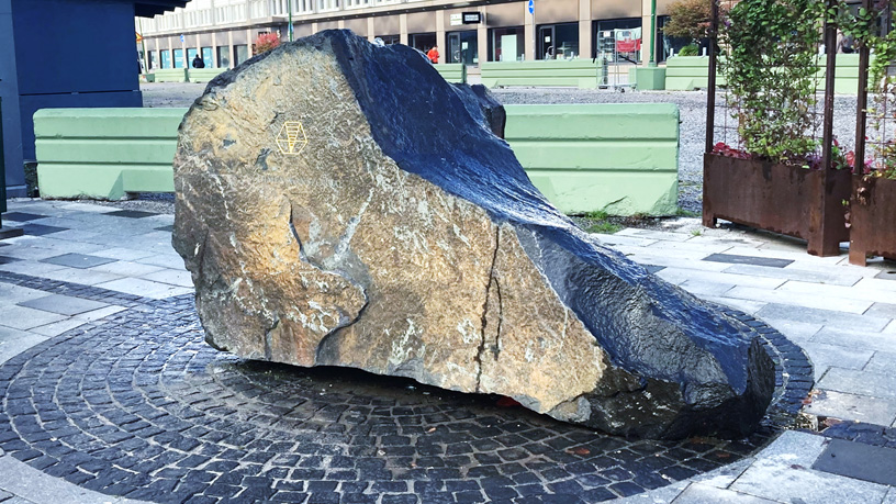 Stor sten på ett torg. Det rinner vatten ur stenen.