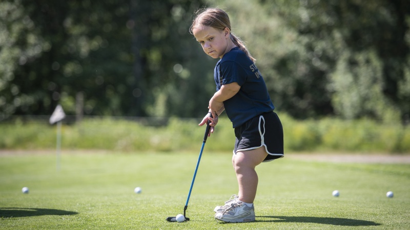 En tjej står på golfbanan med en med golfklubba.