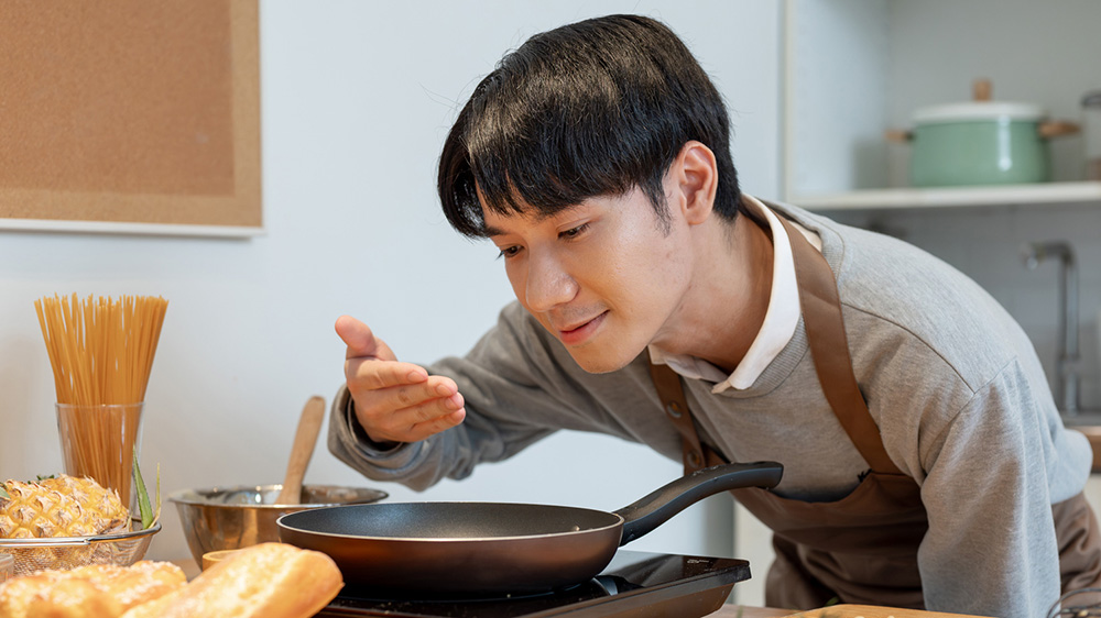 Pojke luktar på något som han tillagar i en stekpanna.